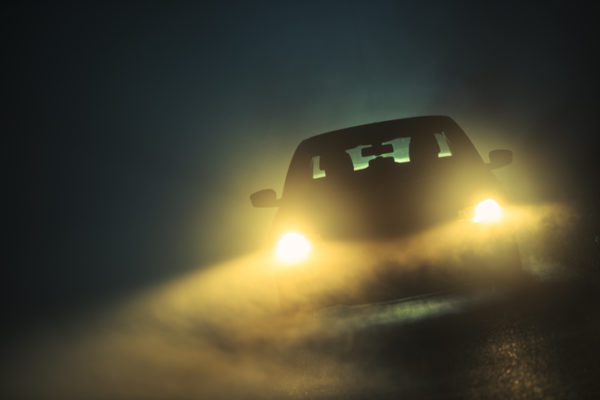 car with headlights on driving through fog at night