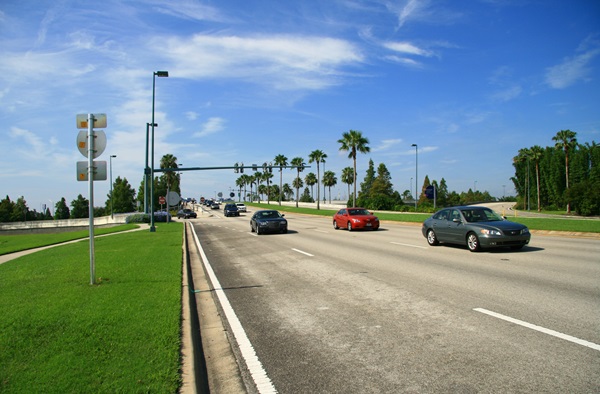 Cars driving down a highway in Florida with palm trees and a blue sky in the background.