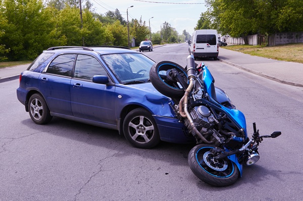 A damaged blue motorcycle lying on top of the front side of a blue car after a collision on a suburban street.